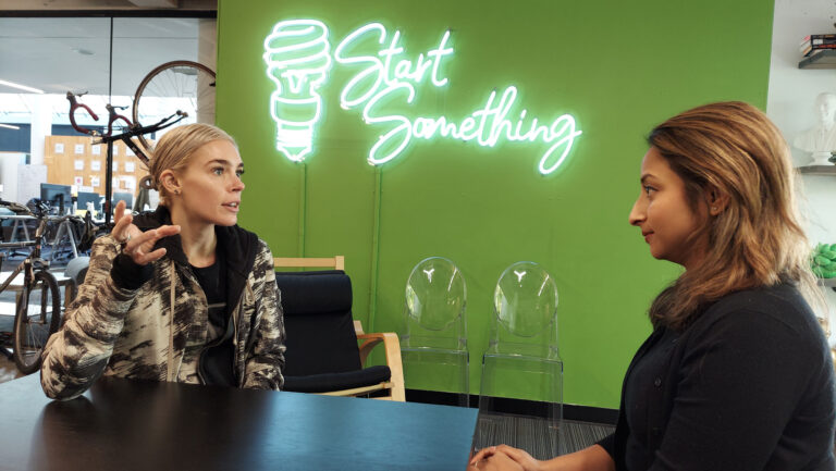 two women meeting with a neon sign on the wall that says "Start Something"