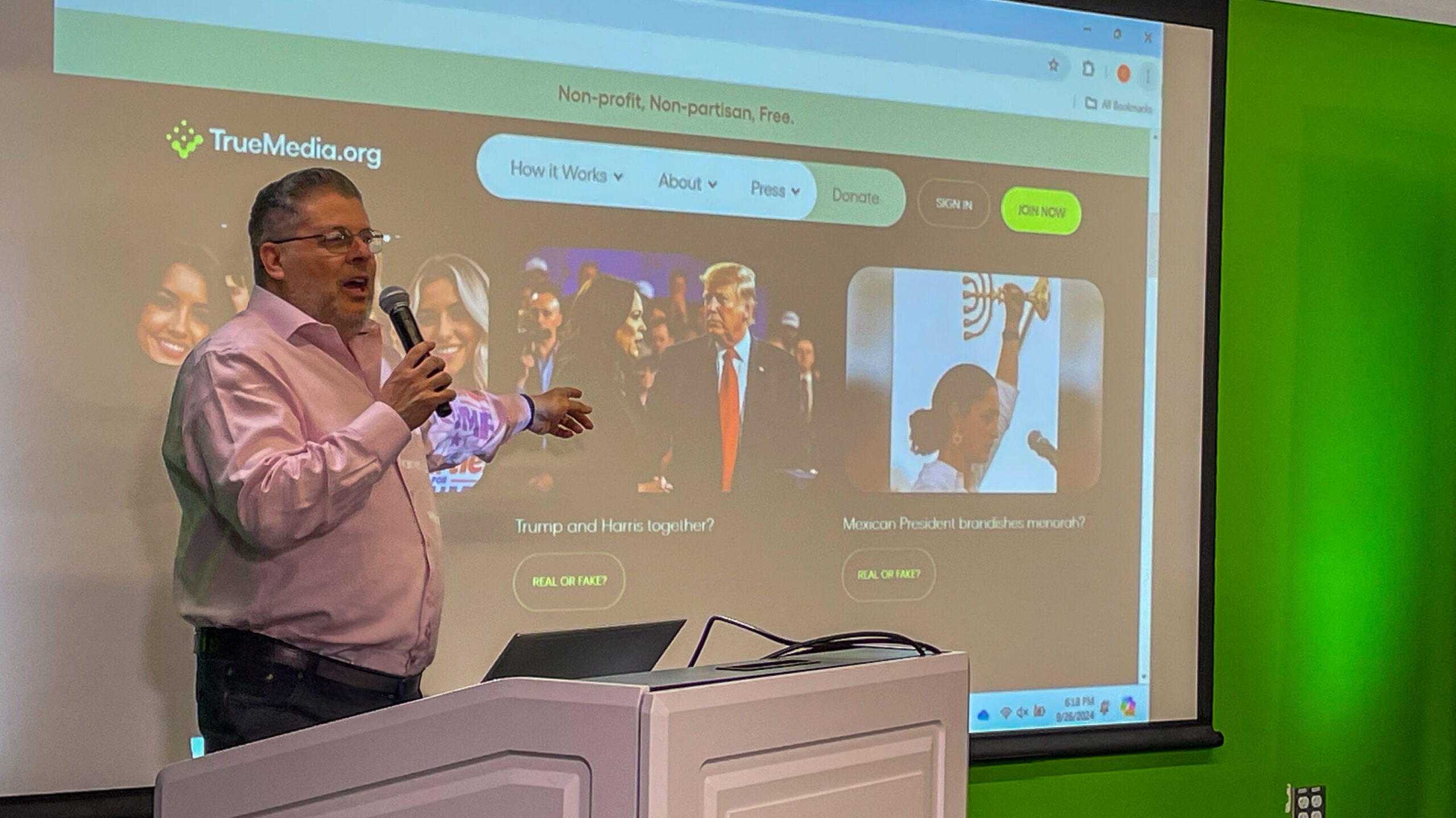 Computer scientist Oren Etzioni stands at a podium in front of a projector screen showing his website, TrueMedia.org