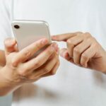 hands hold phone and finger touches screen, as seen from back of phone