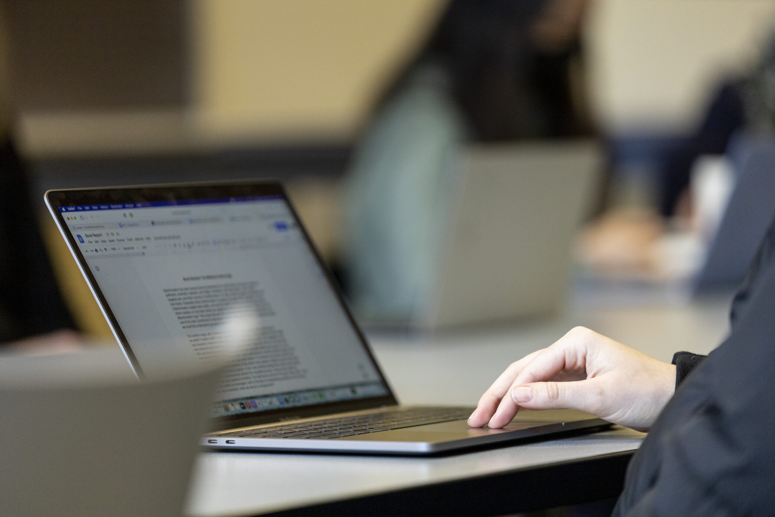Close-up of a student’s hand on a laptop keyboard with a document open on the screen