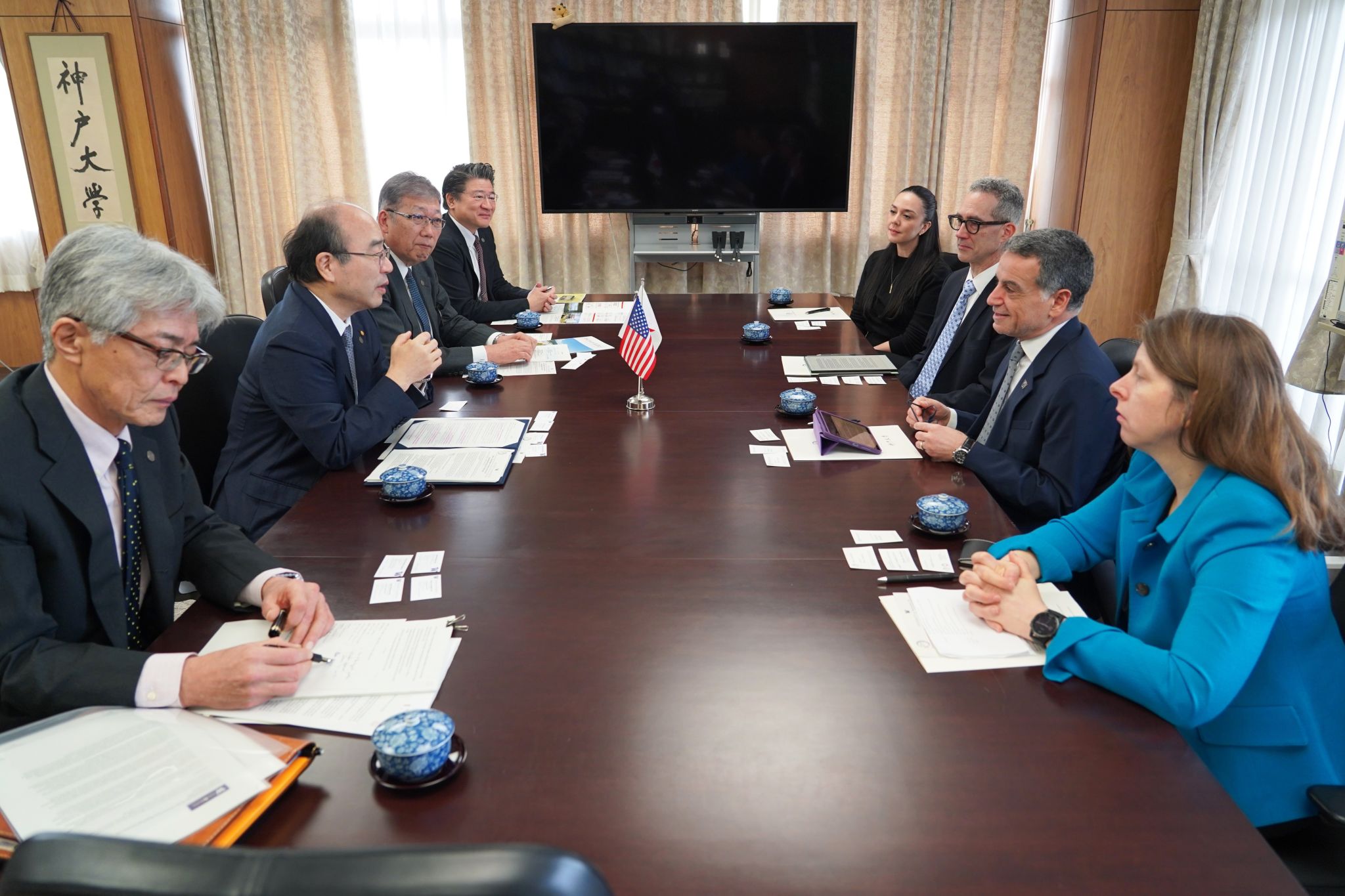 Delegation members from Japan and the United States seated across a conference table during a formal meeting, with a small U.S. flag in the center.