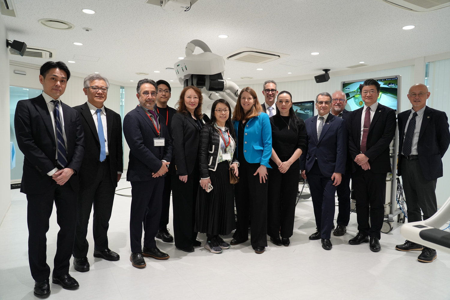 Group of professionals standing in a laboratory with a large medical or research robot and monitors in the background.