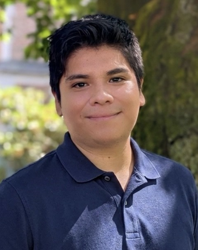 Sergio smiling outdoors in a navy polo shirt beside a tree.