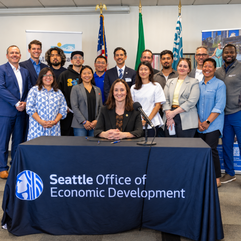 Seattle Mayor Katie Wilson seated at table and partners behind her