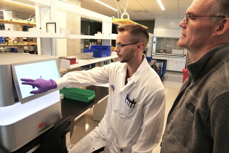 scientists at lab workbench pointing at monitor