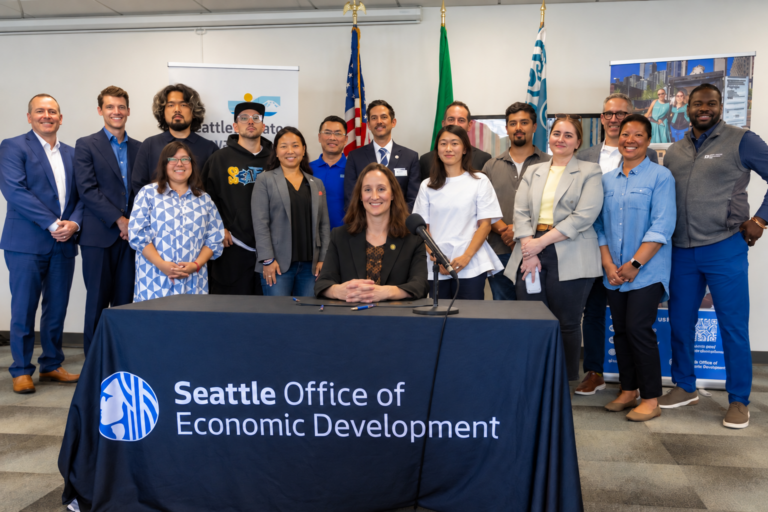 Seattle Mayor Katie Wilson seated at table and partners behind her